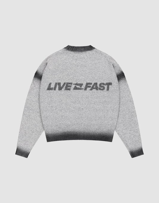 The LIVE FAST DIE YOUNG Live Fast Boucle Sweater features an oversize fit, gray tone, dark gradient cuffs, hem, and collar in a faded spray effect. "LIVE FAST" with a lightning bolt is printed bold on the back. Shown laid flat on a plain background.