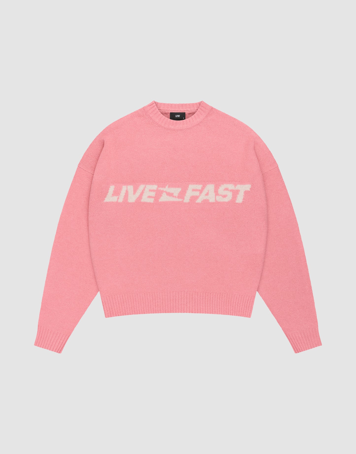 The Live Fast Boucle Sweater by LIVE FAST DIE YOUNG is a pink, oversized knit with bold white "LIVE FAST" lettering across the chest, shown against a plain light background.