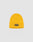 The LFDY Oval Beanie by LFDY is a yellow polyacryl knit hat with a folded brim and a small black oval patch with white text on the front, shown against a plain light gray background.