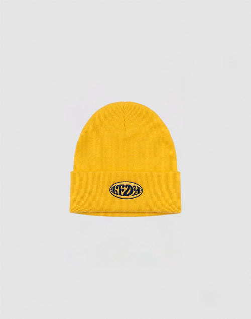 The LFDY Oval Beanie by LFDY is a yellow polyacryl knit hat with a folded brim and a small black oval patch with white text on the front, shown against a plain light gray background.