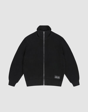 The LFDY Knit Jacket by LIVE FAST DIE YOUNG is a black, ribbed zip-up with Stehkragen, long sleeves, and a small rectangular patch near the hem. Made from 100% Baumwolle, it's shown laid flat on a light gray background. | plain