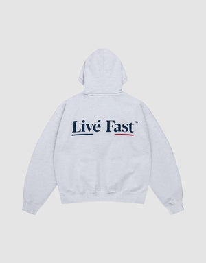 The Live Fast Paris Hooded by LIVE FAST DIE YOUNG is an oversized, light gray cotton hoodie with a bold "Livé Fast" black backprint and red underline, displayed flat on a plain white background. | plain