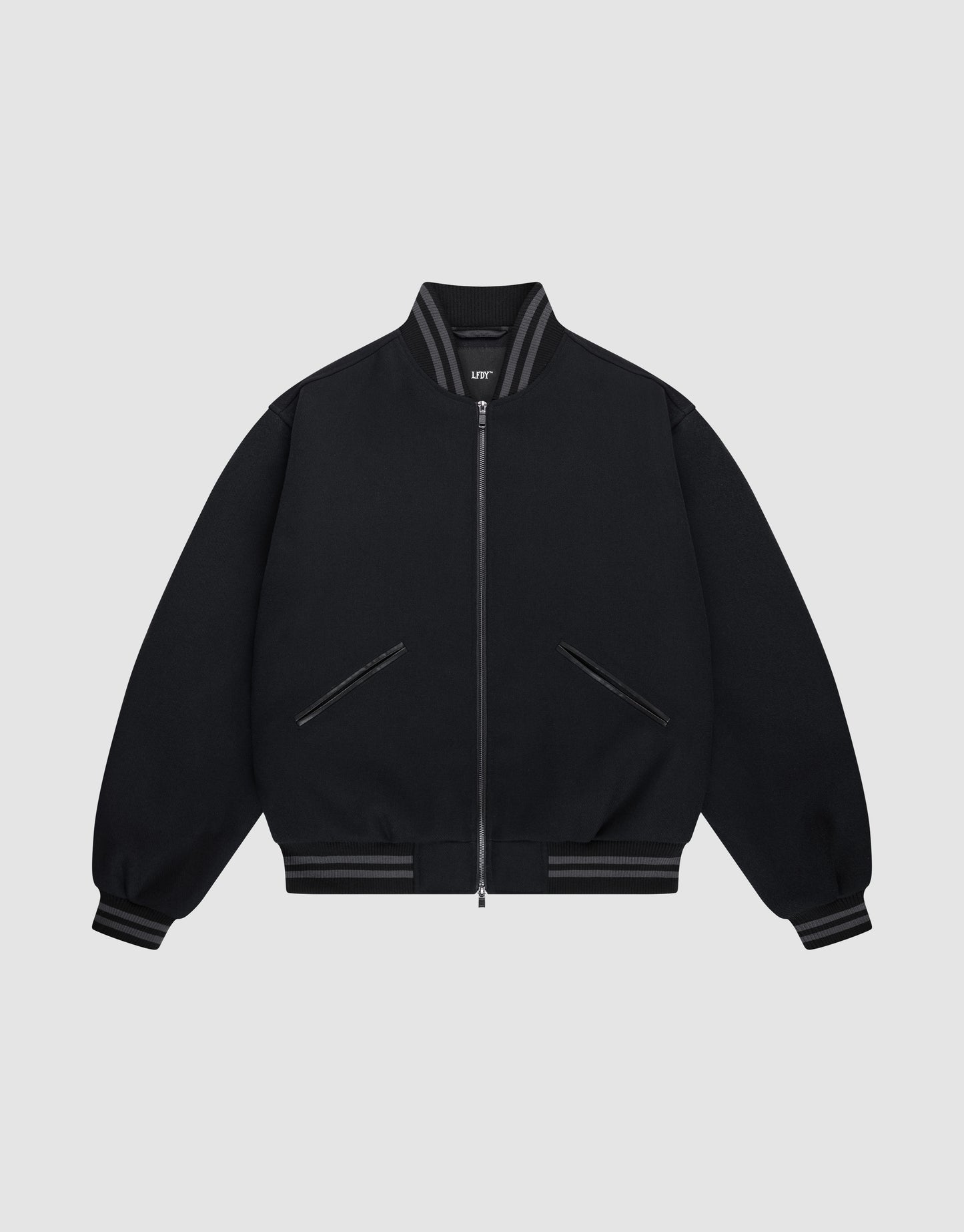 The LIVE FAST DIE YOUNG Live Fast College Jacket is a black varsity zip-up with a Metal Reißverschluss, ribbed gray-striped collar, cuffs, and hem, Logo Applikation on the chest, and two front diagonal zip pockets on a light gray background.