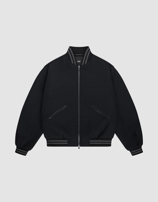 The LIVE FAST DIE YOUNG Live Fast College Jacket is a black varsity zip-up with a Metal Reißverschluss, ribbed gray-striped collar, cuffs, and hem, Logo Applikation on the chest, and two front diagonal zip pockets on a light gray background.