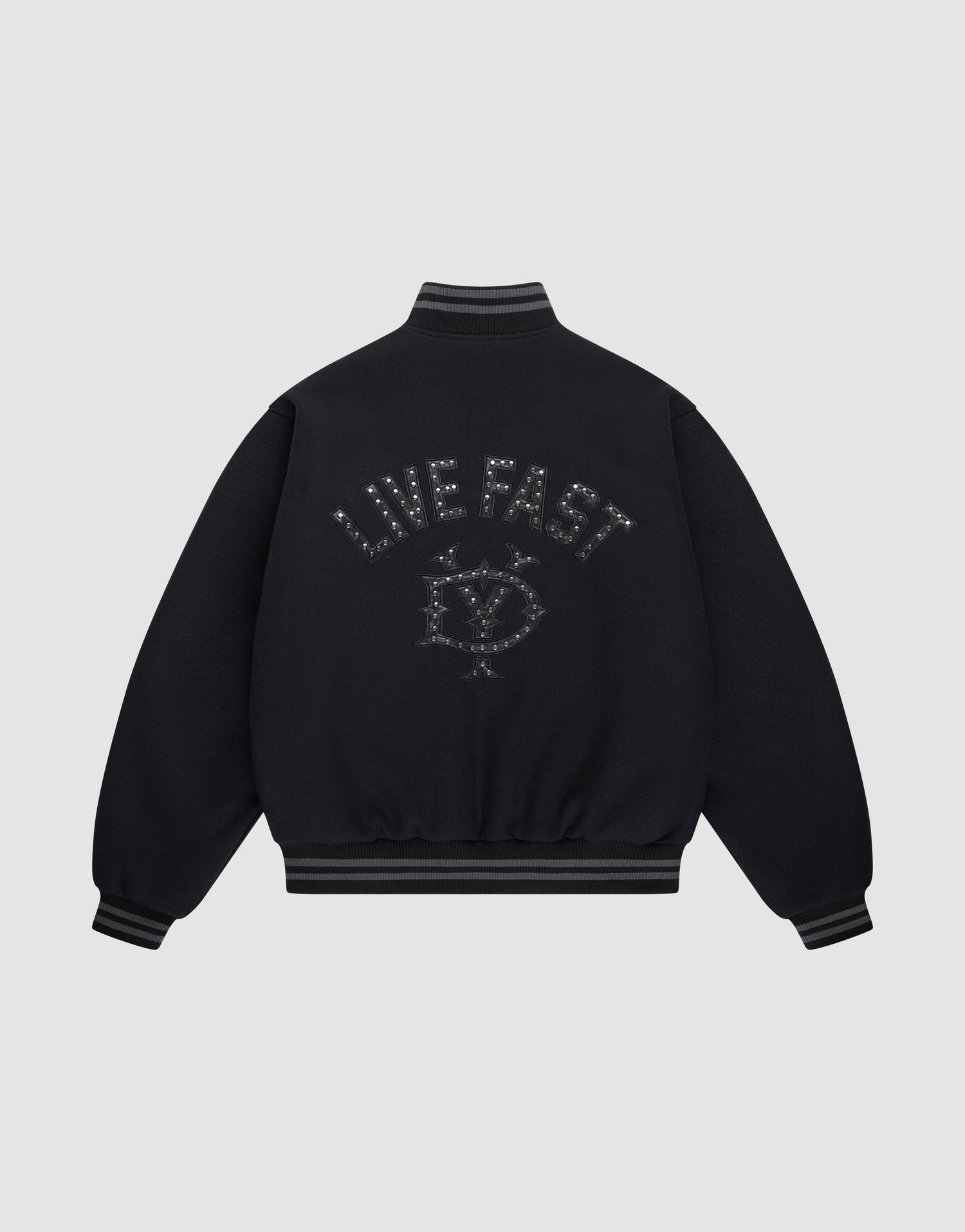 The Live Fast College Jacket by LIVE FAST DIE YOUNG is a black varsity jacket with striped cuffs and hem, a metal zipper, and an embroidered eye with stars and "LIVE FAST" on the back in dark thread. The background is light gray. | plain