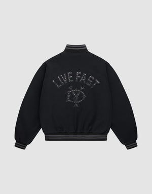 The Live Fast College Jacket by LIVE FAST DIE YOUNG is a black varsity jacket with striped cuffs and hem, a metal zipper, and an embroidered eye with stars and "LIVE FAST" on the back in dark thread. The background is light gray. | plain