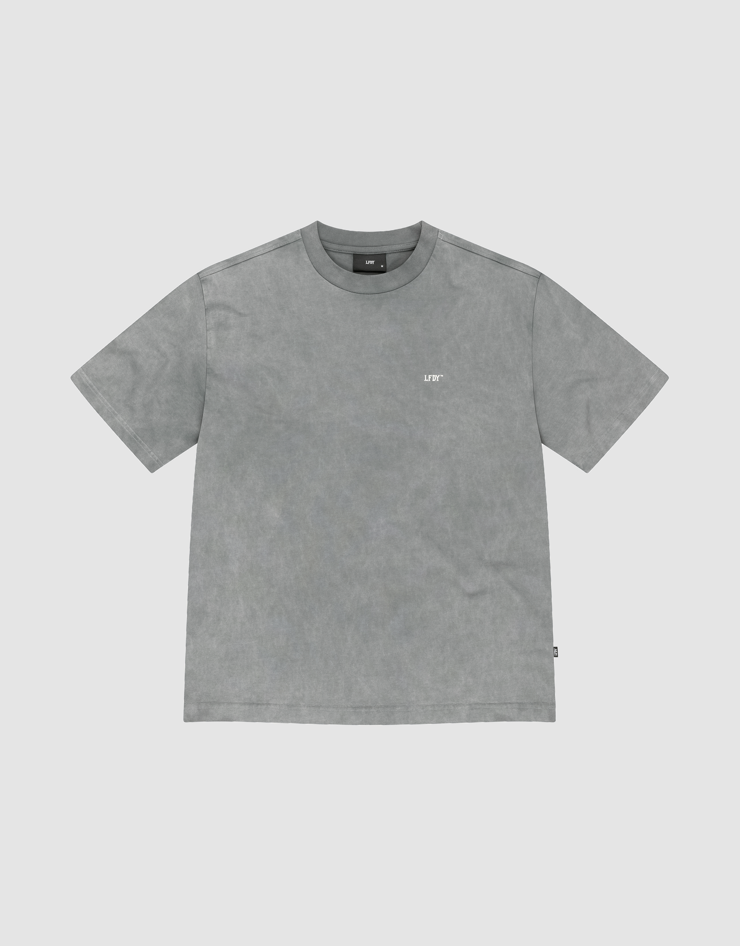 The Basic Trademark Tee by LIVE FAST DIE YOUNG is a gray, short-sleeved crew neck shirt with a small white logo on the upper left chest, made from 100% Baumwolle and displayed flat on a light gray background.