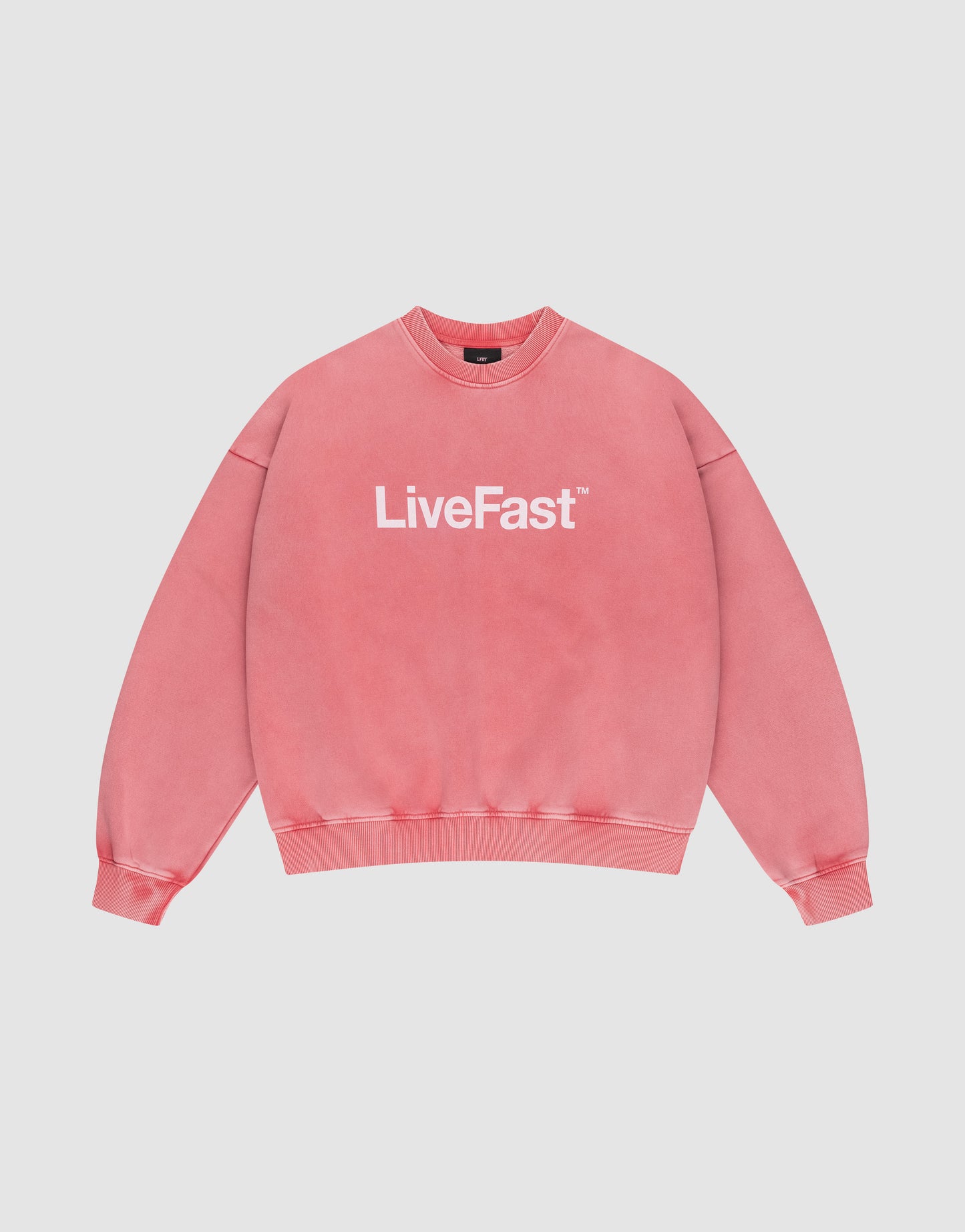 The Basic LiveFast Sweater by LIVE FAST DIE YOUNG is a pink crewneck with "LiveFast™" in bold white on the front, featuring a trendy faded look and shown against a plain light gray background.