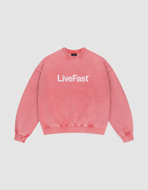 The Basic LiveFast Sweater by LIVE FAST DIE YOUNG is a pink crewneck with "LiveFast™" in bold white on the front, featuring a trendy faded look and shown against a plain light gray background. | plain