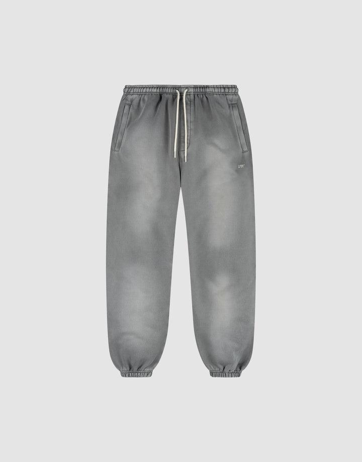 The LIVE FAST DIE YOUNG Basic Loose Jogger is a pair of gray washed sweatpants with a subtle fade effect, elastic waistband and white drawstring, side pockets, and elastic ankle cuffs, shown on a plain light background. | plain
