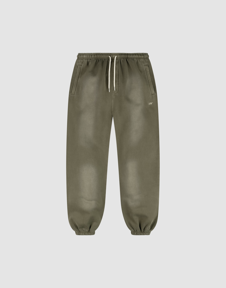 The LIVE FAST DIE YOUNG Basic Loose Jogger features olive green fabric with a handgefertigter Fade-Effekt, an elastic waistband with a white drawstring, side pockets, elastic ankle cuffs, and a small white logo near the left pocket. | plain