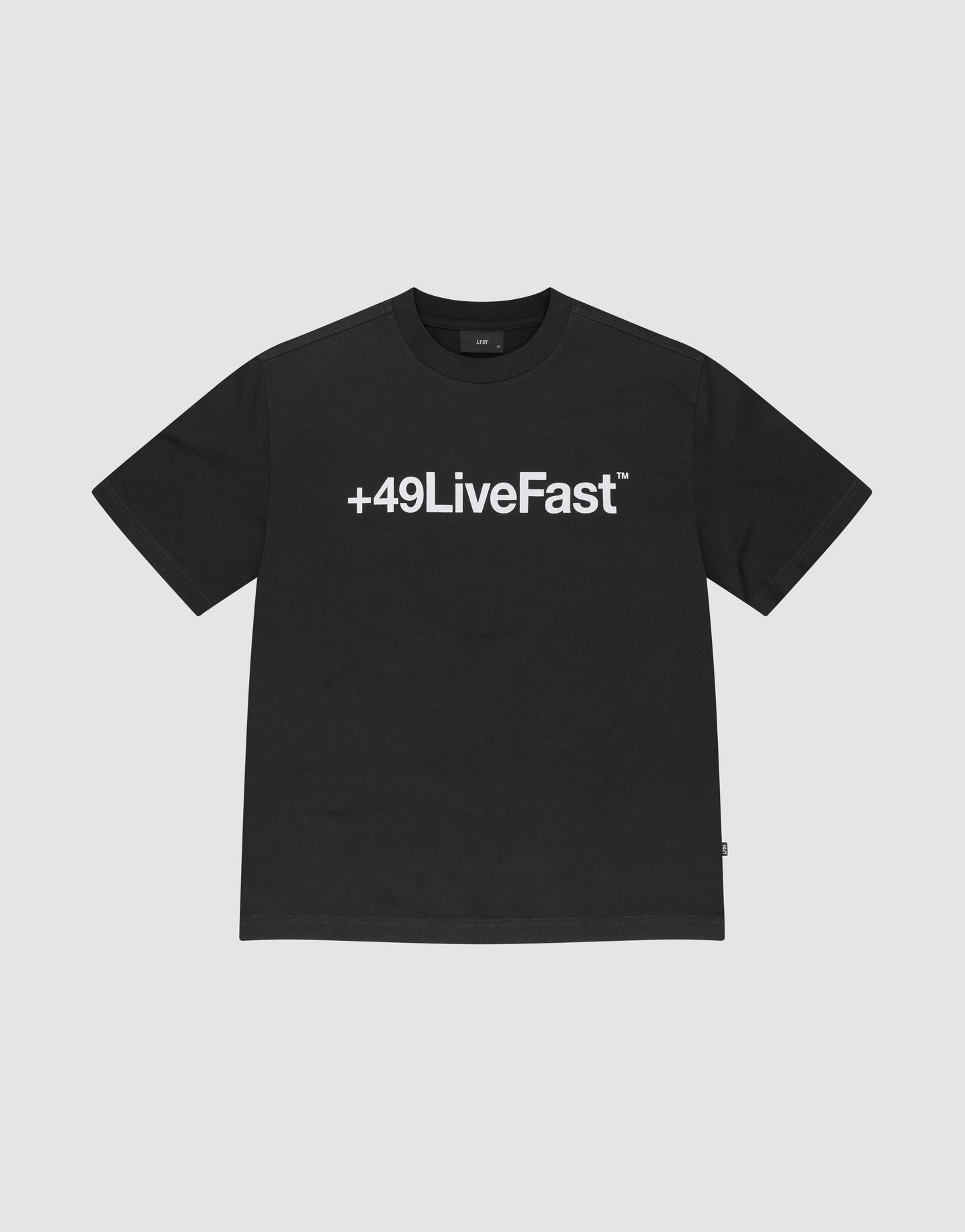 The Basic +49 Tee by LIVE FAST DIE YOUNG features a bold white +49LiveFast™ print across the chest, made from 100% cotton in an oversized fit, shown on a plain light grey background.