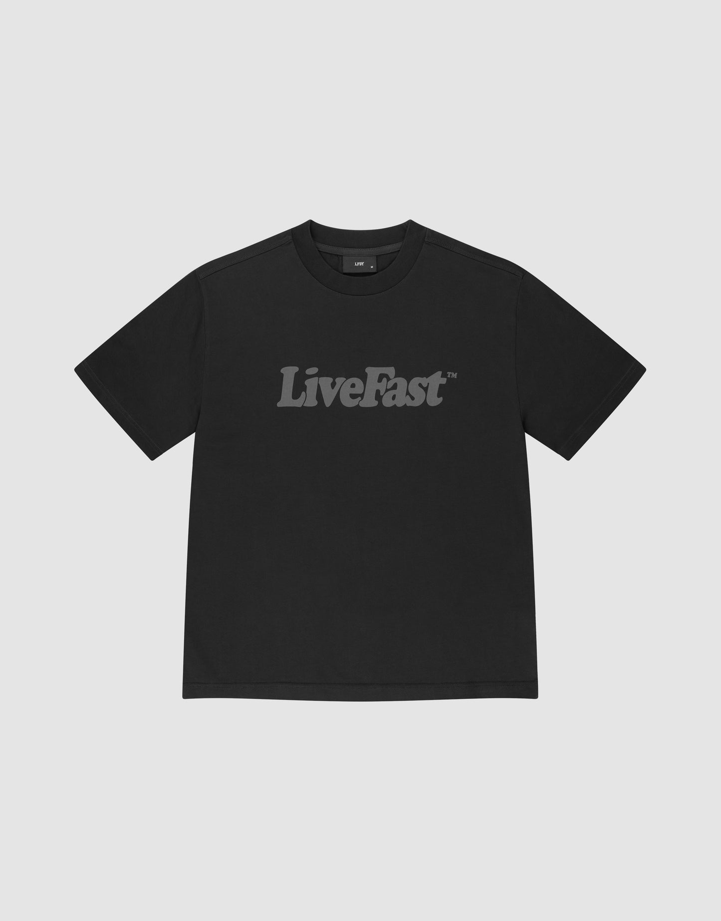 The LIVE FAST DIE YOUNG Basic Tee is a black, oversize fit t-shirt made from 100% Baumwolle, featuring "LiveFast" in bold gray letters across the chest and shown on a plain light gray background.