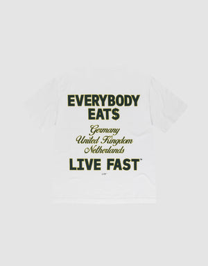 The Everybody Eats Tee by LIVE FAST DIE YOUNG is a white oversized cotton T-shirt with bold black and yellow front and back prints reading "EVERYBODY EAT$ Germany United Kingdom Netherlands LIVE FAST™," shown flat on a light gray background. | plain