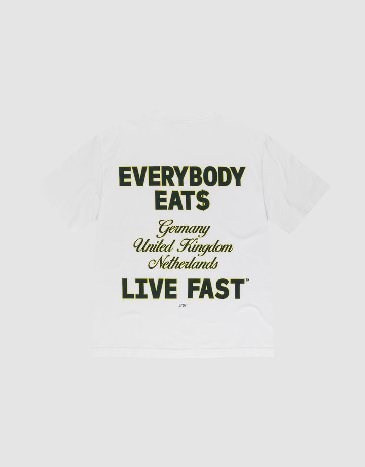 The Everybody Eats Tee by LIVE FAST DIE YOUNG is a white oversized cotton T-shirt with bold black and yellow front and back prints reading "EVERYBODY EAT$ Germany United Kingdom Netherlands LIVE FAST™," shown flat on a light gray background. | plain