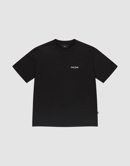 The Live Fast Paris Tee by LIVE FAST DIE YOUNG is a plain black Regular Fit short-sleeve t-shirt made from 100% Baumwolle, featuring a small white LMC Bar logo on the left chest, shown on a light gray background.