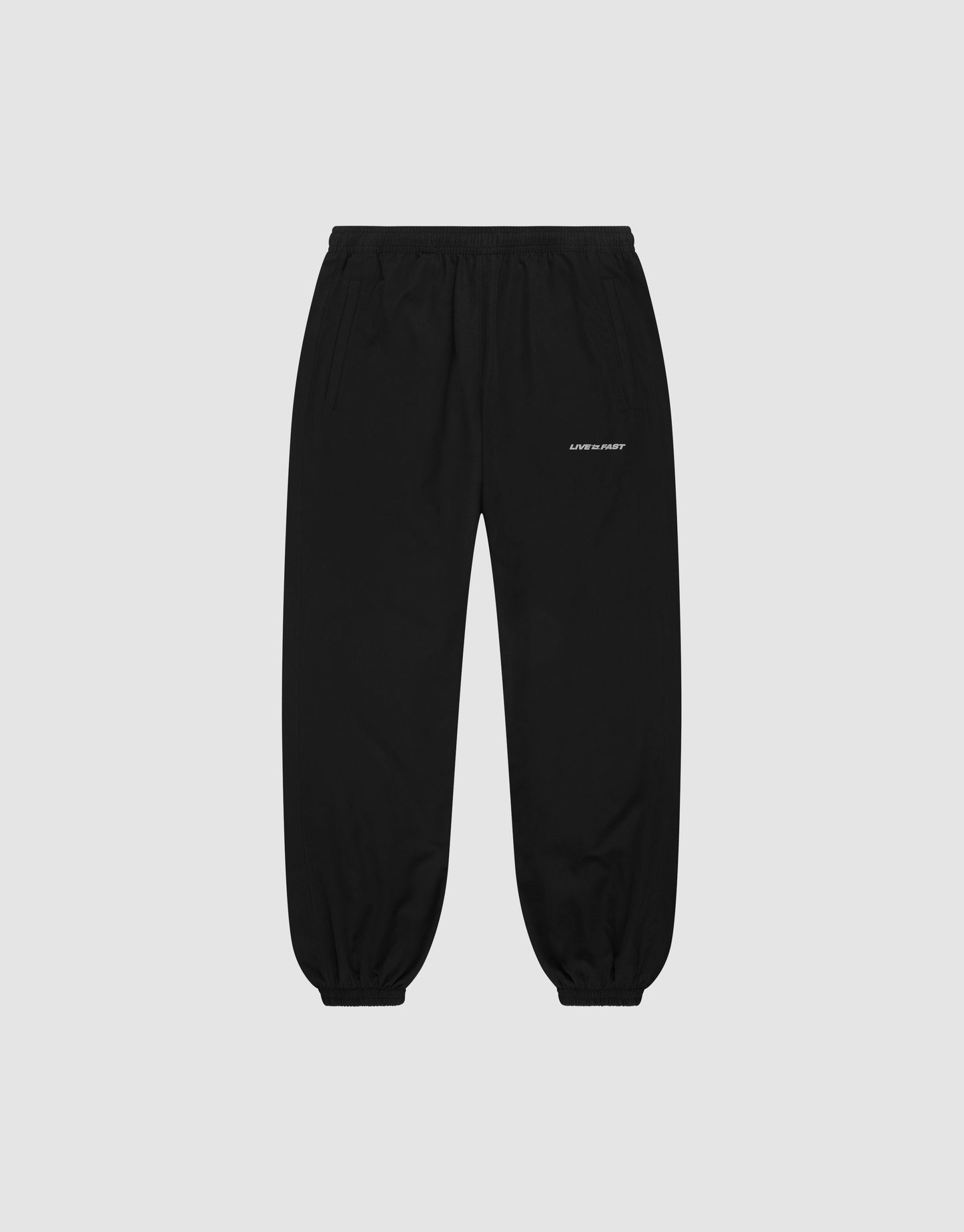 LFDY Trackpants by LIVE FAST DIE YOUNG: black regular-fit joggers with elastic waistband and cuffs, side pockets, and a small white logo on the upper left thigh, shown on a plain light grey background.