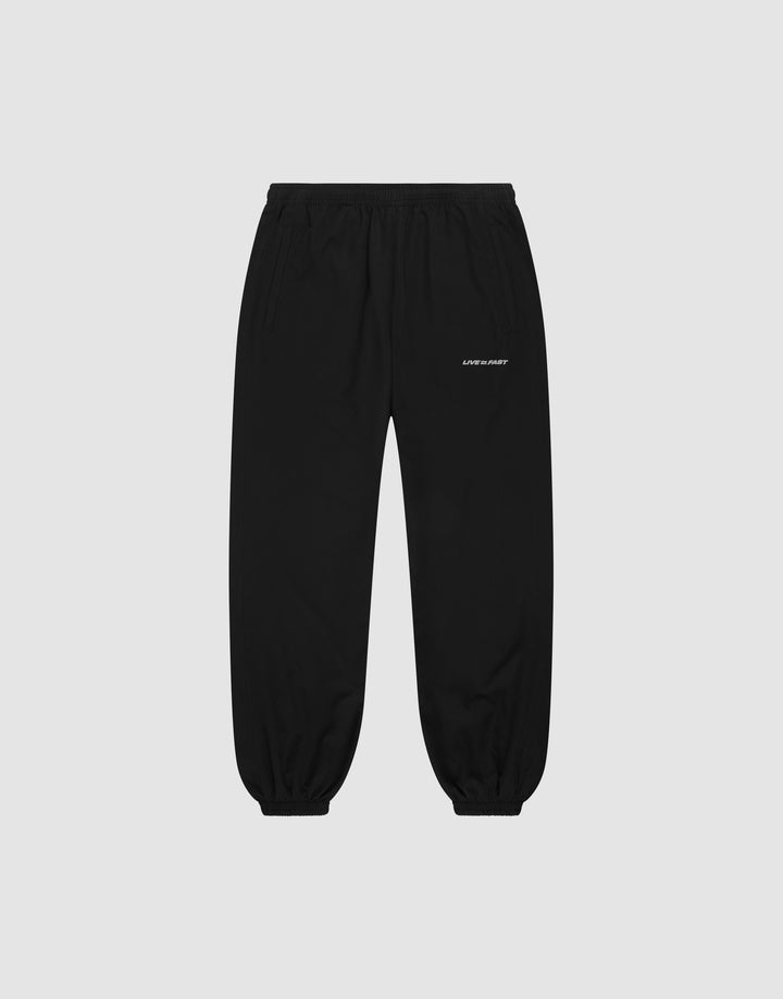 LFDY Trackpants by LIVE FAST DIE YOUNG: black regular-fit joggers with elastic waistband and cuffs, side pockets, and a small white logo on the upper left thigh, shown on a plain light grey background. | plain