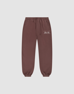 Die braune Wide Cuff Jogger von LIVE FAST DIE YOUNG aus French Terry hat Elastikbund, Seitentaschen, weiße Prints und Logo am linken Oberschenkel und ist vor grauem Hintergrund präsentiert. | plain