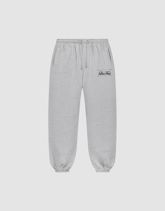 Light gray Wide Cuff Jogger sweatpants by LIVE FAST DIE YOUNG with a wide fit, elastic waistband with drawstring, side pockets, and elastic cuffs. Small black script logo on left thigh. Shown on a plain white background. | plain