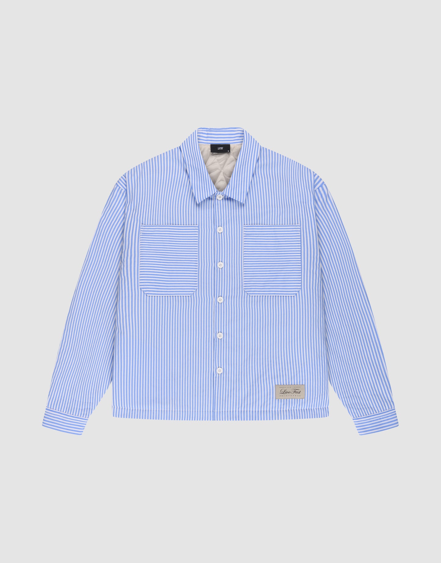 The LFDY Striped Padded Shirt by LIVE FAST DIE YOUNG features blue and white vertical stripes, an oversize fit, long sleeves, two front chest pockets, and a small rectangular label near the lower left hem. Displayed on a plain light background.