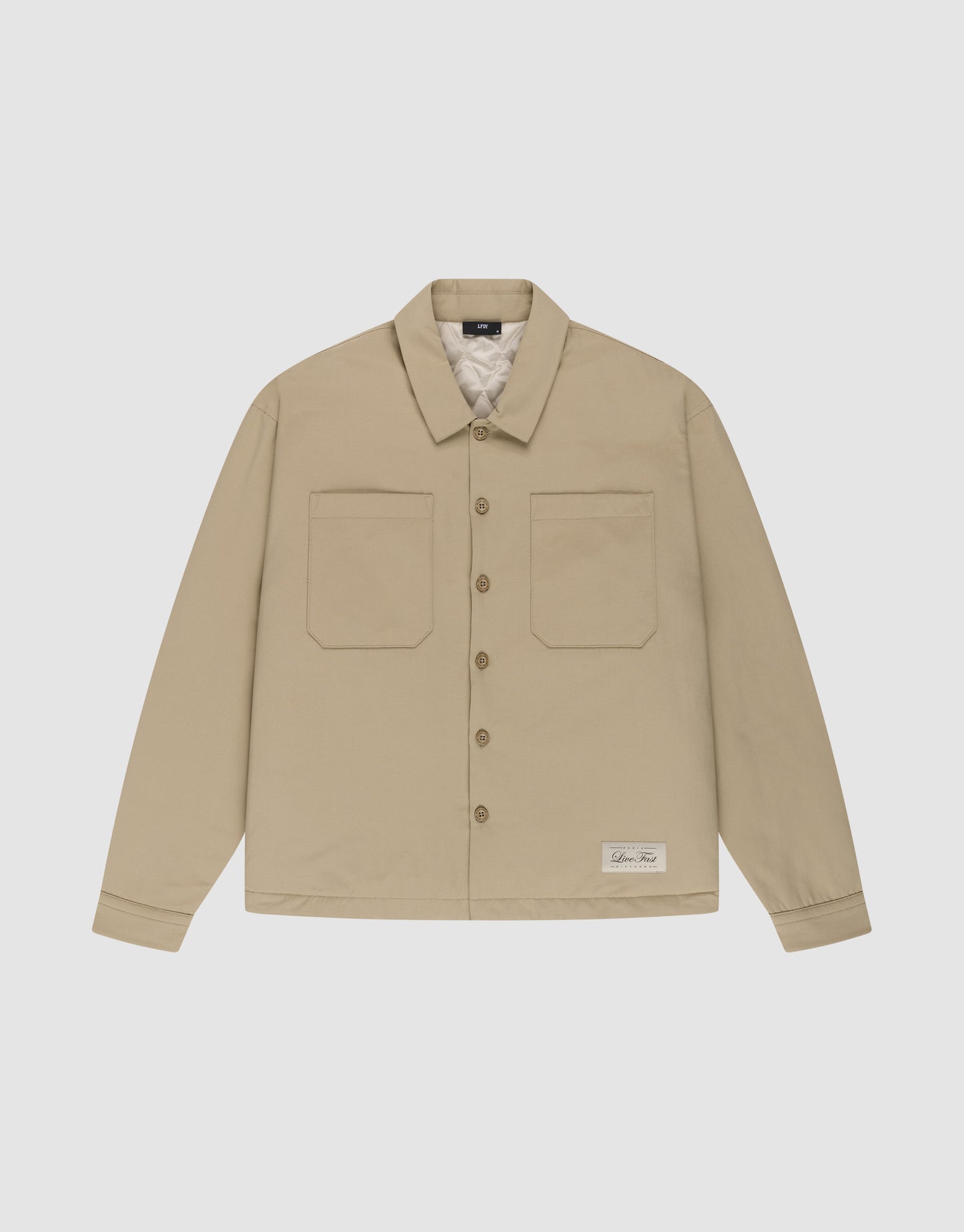 The LFDY Padded Shirt by LIVE FAST DIE YOUNG is a beige, padded overshirt with two front chest pockets, a collar, and a white label near the left hem, shown on a white background.