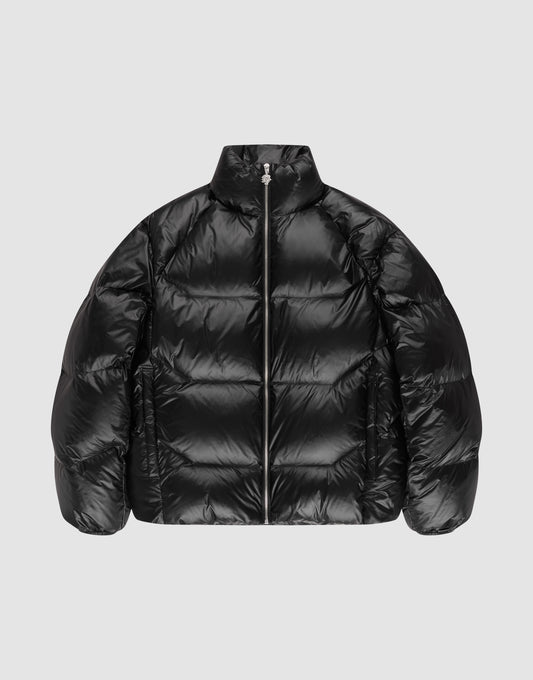 The LIVE FAST DIE YOUNG Live Fast Down Jacket is a shiny black oversized Daunenjacke with 600er Fillpower, high collar, front zipper, and quilted sections, shown against a plain light gray background. | plain
