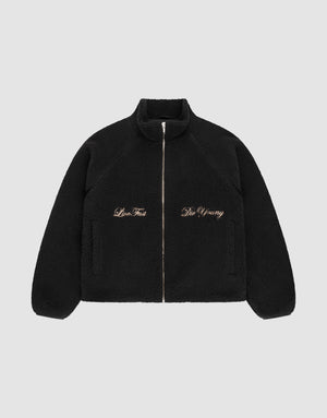 The LFDY Teddy Jacket by LIVE FAST DIE YOUNG is a black fleece jacket with raglan sleeves, side pockets, and gold "Live Fast" and "Die Young" embroidery on the chest, shown on a plain light gray background. | plain