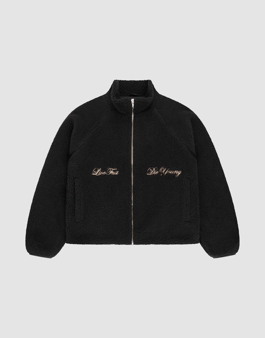 The LFDY Teddy Jacket by LIVE FAST DIE YOUNG is a black fleece jacket with raglan sleeves, side pockets, and gold "Live Fast" and "Die Young" embroidery on the chest, shown on a plain light gray background. | plain
