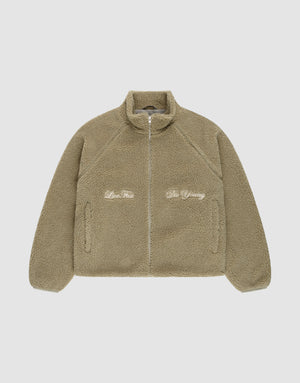 The LFDY Teddy Jacket by LIVE FAST DIE YOUNG is a tan oversized fleece jacket with a high collar and raglan sleeves. Embroidered text "Live Fast" appears on the left and "Die Young" on the right, shown laid flat on a white background. | plain