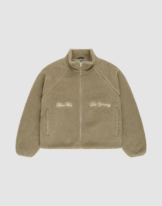 The LFDY Teddy Jacket by LIVE FAST DIE YOUNG is a tan oversized fleece jacket with a high collar and raglan sleeves. Embroidered text "Live Fast" appears on the left and "Die Young" on the right, shown laid flat on a white background. | plain