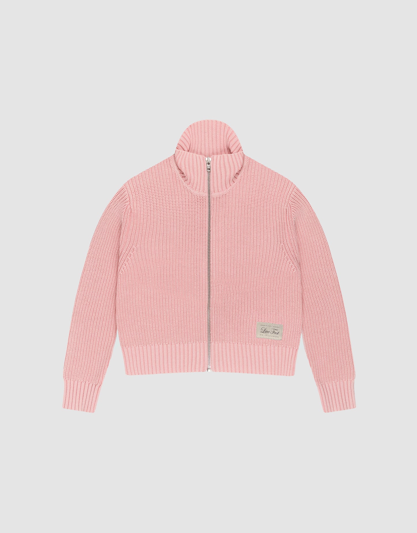 The LFDY Knit Jacket by LIVE FAST DIE YOUNG is a light pink, ribbed zip-up sweater with a stand collar and long sleeves, made from 100% cotton. A small beige patch accents the lower left front. Shown here laid flat on a white background.