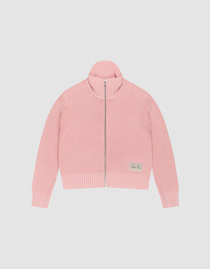 The LFDY Knit Jacket by LIVE FAST DIE YOUNG is a light pink, ribbed zip-up sweater with a stand collar and long sleeves, made from 100% cotton. A small beige patch accents the lower left front. Shown here laid flat on a white background. | plain