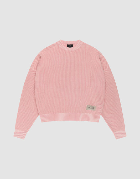The LFDY Knit Sweater by LIVE FAST DIE YOUNG features pink ribbed knit, an oversized fit, dropped shoulders, long sleeves, a crew neckline, and a small rectangular beige patch with text on the front hem, displayed on a plain white background. | plain