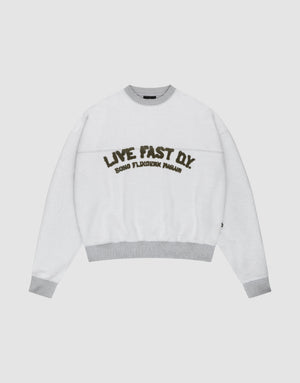 The LFDY District Sweater by LIVE FAST DIE YOUNG is a white oversized crewneck with light gray collar, cuffs, and hem in 480 GSM inside-out fabric. The chest displays bold LIVE FAST D.I.Y. text above ROAD FLECHTERIN PARADIS. | plain