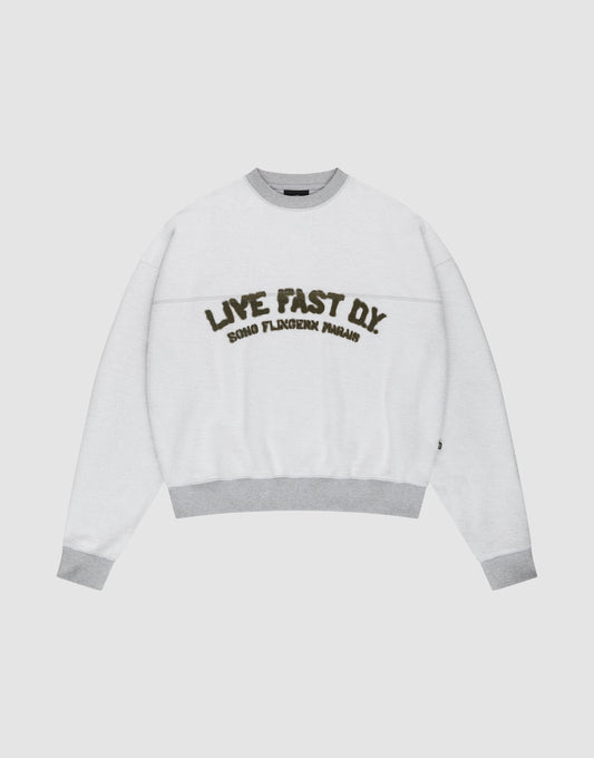 The LFDY District Sweater by LIVE FAST DIE YOUNG is a white oversized crewneck with light gray collar, cuffs, and hem in 480 GSM inside-out fabric. The chest displays bold LIVE FAST D.I.Y. text above ROAD FLECHTERIN PARADIS. | plain