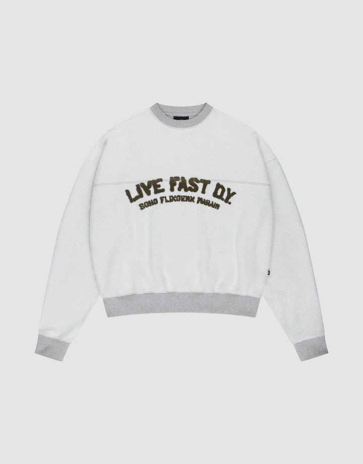 The LFDY District Sweater by LIVE FAST DIE YOUNG is a white oversized crewneck with light gray collar, cuffs, and hem in 480 GSM inside-out fabric. The chest displays bold LIVE FAST D.I.Y. text above ROAD FLECHTERIN PARADIS. | plain