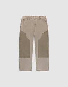 The LIVE FAST DIE YOUNG Faded Carpenter Pants are beige, straight-leg, baggy-fit jeans with large darker beige patches on the front thigh and knee, featuring front pockets and belt loops, displayed flat on a light background. | plain