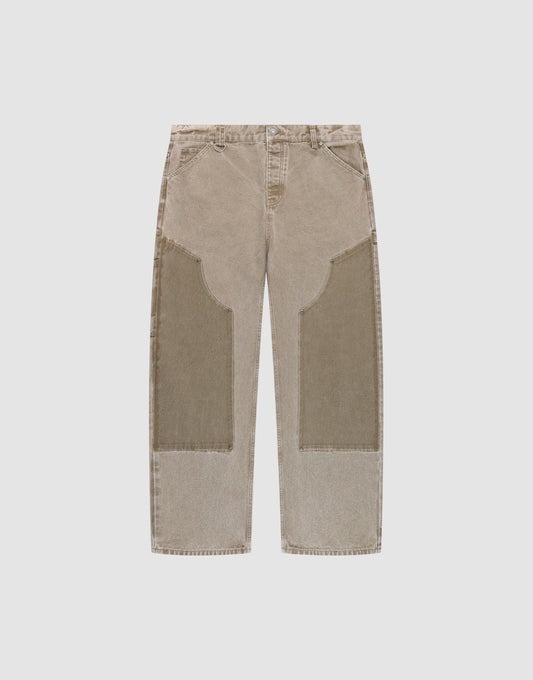 The LIVE FAST DIE YOUNG Faded Carpenter Pants are beige, straight-leg, baggy-fit jeans with large darker beige patches on the front thigh and knee, featuring front pockets and belt loops, displayed flat on a light background. | plain