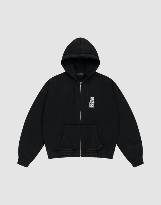The LIVE FAST DIE YOUNG Live Fast Lenox Hooded Zip is a black oversized cotton hoodie with a zip-up front, hood, and front pockets, featuring a white LIVE FAST logo on the left chest, shown on a light gray background.