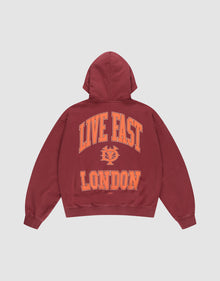 The LIVE FAST DIE YOUNG "Live Fast London Hooded Zip" is a maroon, oversized 100% Baumwolle hoodie with a hood and large orange “LIVE FAST LONDON” text plus an emblem on the back. Shown on a plain white background. | plain