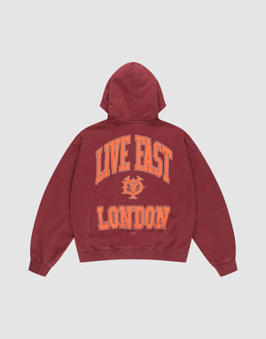 The LIVE FAST DIE YOUNG "Live Fast London Hooded Zip" is a maroon, oversized 100% Baumwolle hoodie with a hood and large orange “LIVE FAST LONDON” text plus an emblem on the back. Shown on a plain white background. | plain