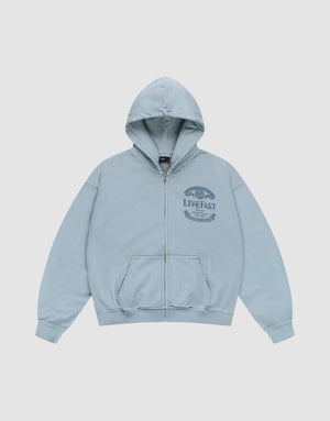 The LFDY 55 Hooded Zip by LIVE FAST DIE YOUNG is a light blue, oversized zip-up hoodie with a front pocket, hood, and dark blue LIVE FAST graphic with laurel wreath on the left chest. Made from 100% Baumwolle. Shown laid flat on a white background. | plain