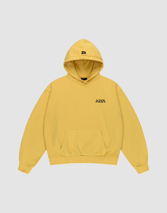 The Print Over Hooded by LIVE FAST DIE YOUNG is an oversized yellow hoodie with a front pocket, small black LIVE logo on the chest, black graphic on the hood, and is made from 100% cotton. Shown on a plain light gray background.