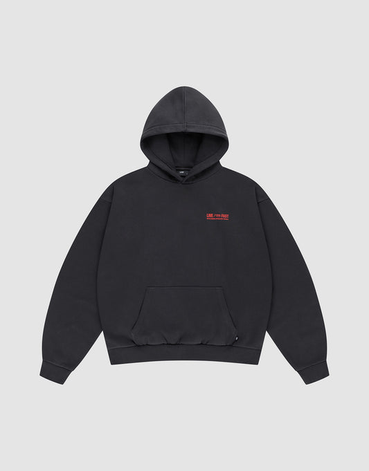 The LIVE FAST DIE YOUNG Hit and Run Hooded is a plain black oversized sweatshirt with a front pouch pocket and small red text discharge print on the left chest, shown on a light gray background.