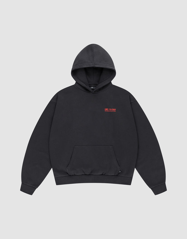 The LIVE FAST DIE YOUNG Hit and Run Hooded is a plain black oversized sweatshirt with a front pouch pocket and small red text discharge print on the left chest, shown on a light gray background.