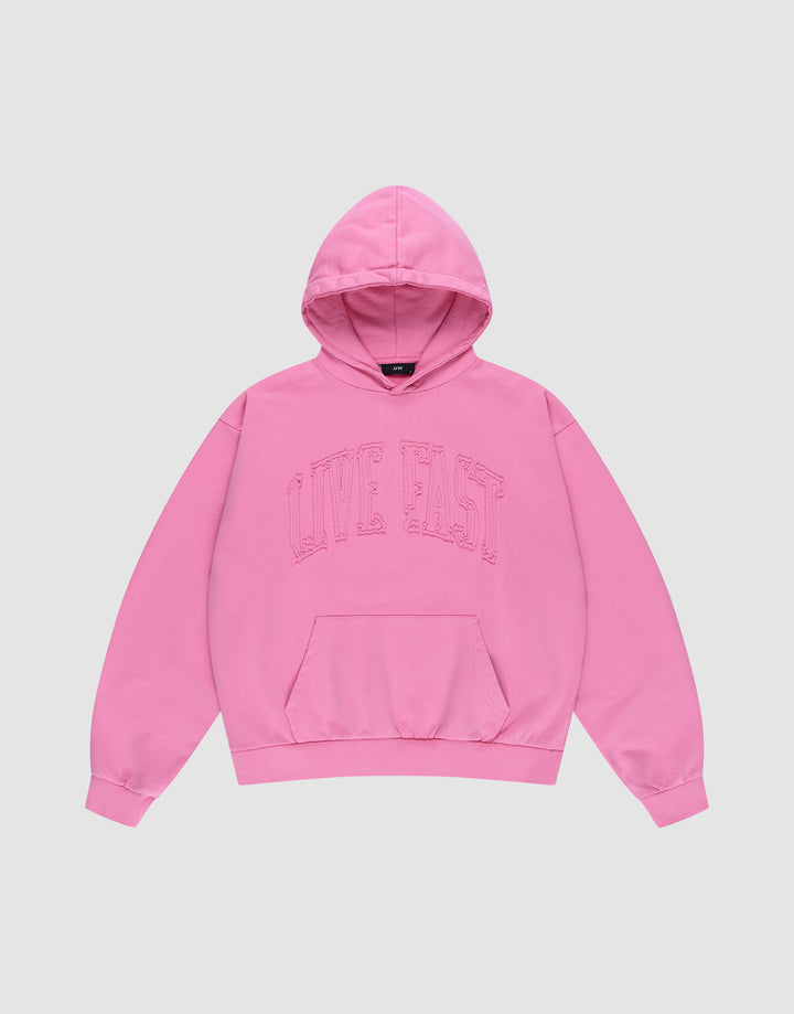 The Ripped College Hooded by LIVE FAST DIE YOUNG is a bright pink oversized hoodie made from 100% Baumwolle, featuring a front pocket and bold "LIVE FAST" lettering across the chest, shown laid flat on a plain light background. | plain