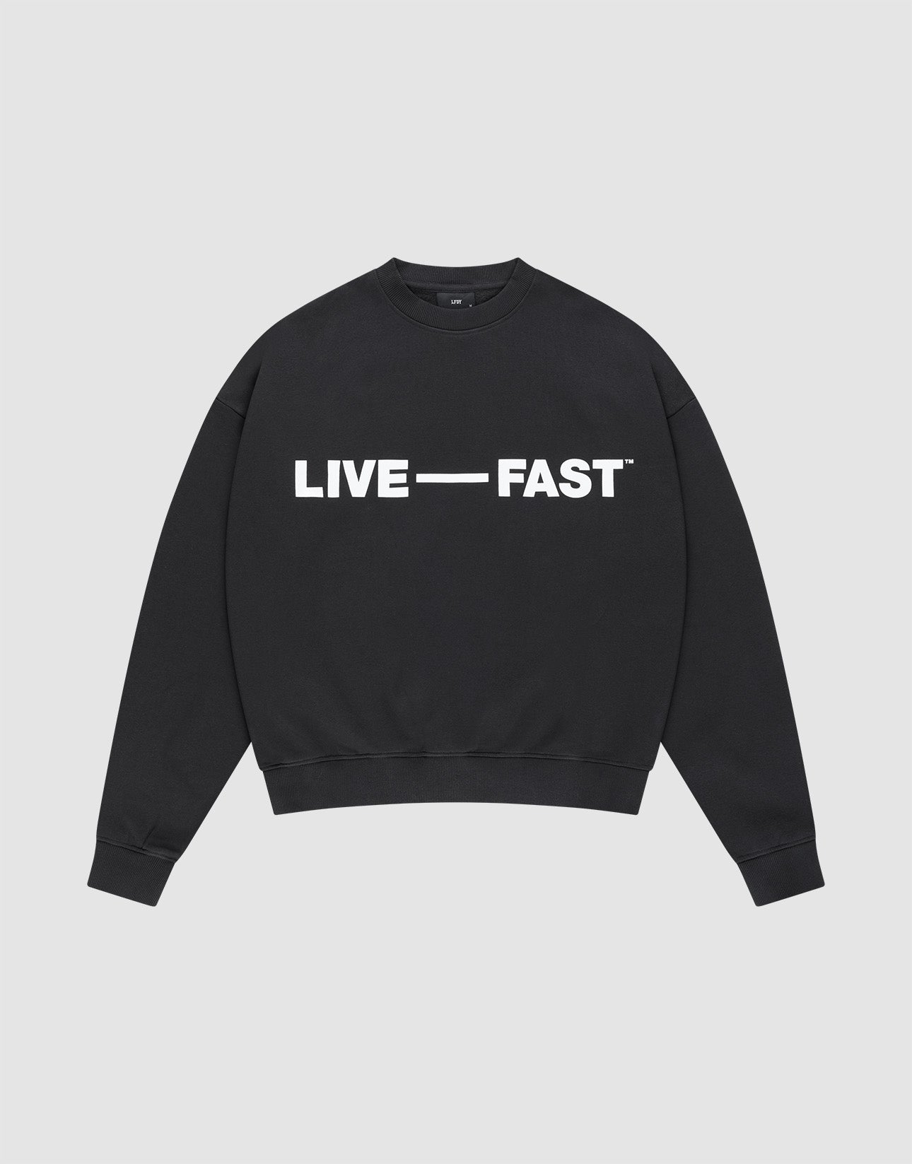 The Live – Fast Sweater by LIVE FAST DIE YOUNG is a black, oversized crewneck cotton pullover with "LIVE — FAST" in bold white glossy silicone print on the chest, shown laid flat against a plain light gray background. | plain