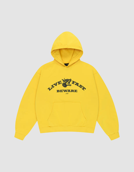 The Live Fast Beware Hooded by LIVE FAST DIE YOUNG is an oversize yellow hoodie made of 100% Baumwolle, featuring black "LIVE FAST. BEWARE" text and a horned skull illustration on the chest, set against a light gray background.