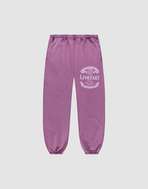 Die Loyal Loose Jogger von LIVE FAST DIE YOUNG sind lila Jogginghosen aus Baumwolle mit elastischem Bund und Bündchen, Vintage-Waschung und weißem LIVE FAST-Print am Oberschenkel, präsentiert vor grauem Hintergrund. | plain